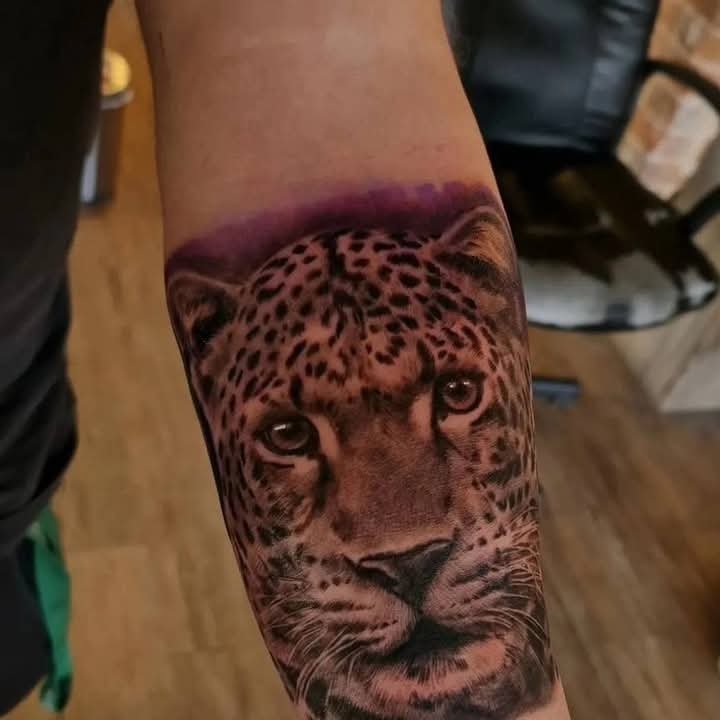 Realistic color leopard face tattoo on a forearm