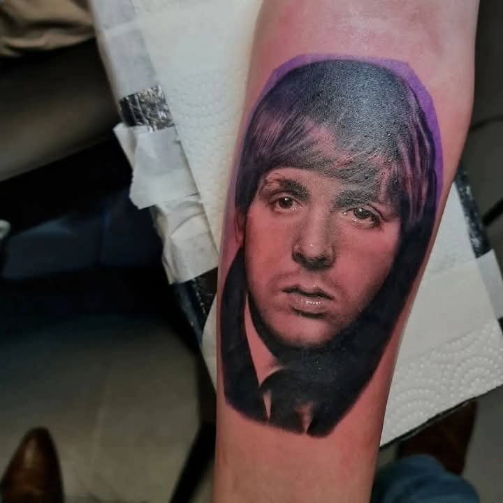 Realistic portrait tattoo with purple ornamental accents on an arm