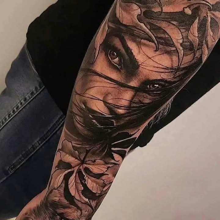 Black and grey surreal woman portrait tattoo with botanical leaves on a forearm