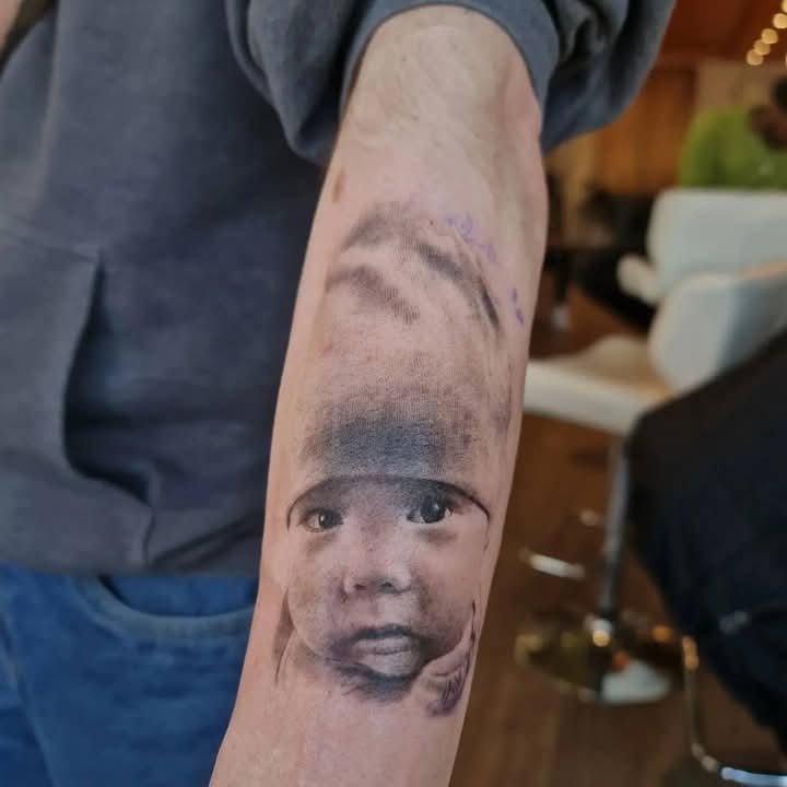 Black and grey realistic child portrait tattoo on a forearm